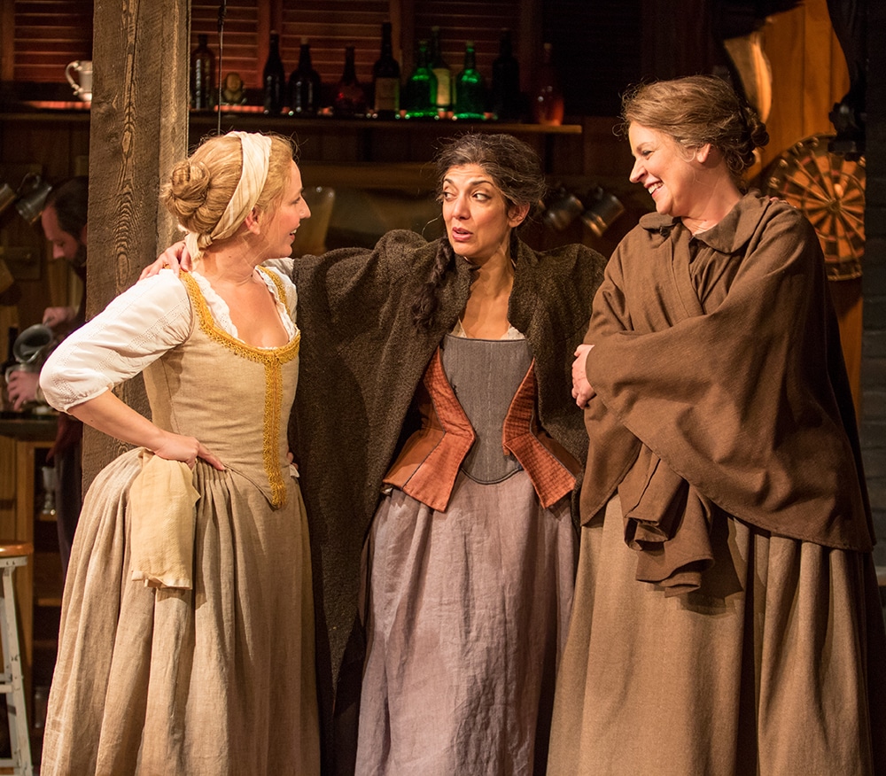 Three women in renaissance dresses converse in a light-hearted conversation.