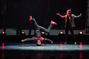 A hip hop dancer dressed in red and black spins on his head.