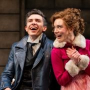 A man in a blue leather jacket laughs with a woman in a pink jacket.
