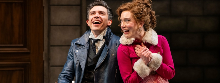 A man in a blue leather jacket laughs with a woman in a pink jacket.