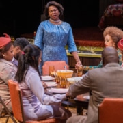 Chavez Ravine stands at the head of a table and prays with the cast of In the Upper Room, all dressed in their Sunday best