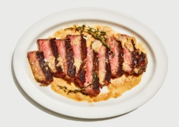 A seared steak cut into slices on a white tray