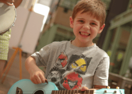 A child smiles while holding a small blue guitar