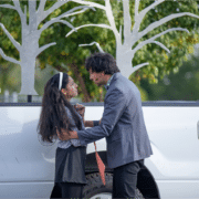 Actor in a silvery blue blazer holds Actress in a white sweater and headband as they exchange deep and heart felt looks