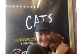 A woman holds her dog in front of the CATS show poster
