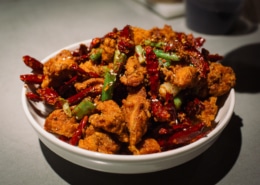 A bowl of Chinese food with meat, green onions, and peppers
