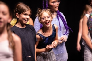 Two children smile and laugh onstage during a performance