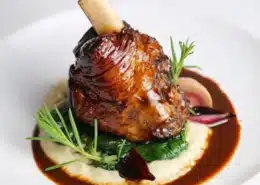 A lamb shank surrounded by sauce and herbs