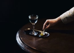 A glass sits on a tray while a hand reaches for it