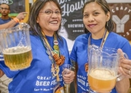 Two volunteers stand together for a photo holding pitchers of beer