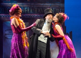 Two women lean in to kiss a man's cheeks in My Fair Lady