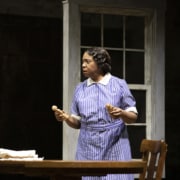 Calpurnia stands at a table holding wooden dolls in To Kill a Mockingbird