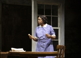 Calpurnia stands at a table holding wooden dolls in To Kill a Mockingbird