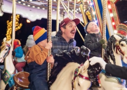 A man shouts with joy with his children as they ride the carousel at Camp Christmas