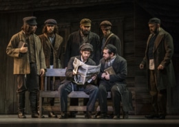 A group of men surround a newspaper in Fiddler on the Roof