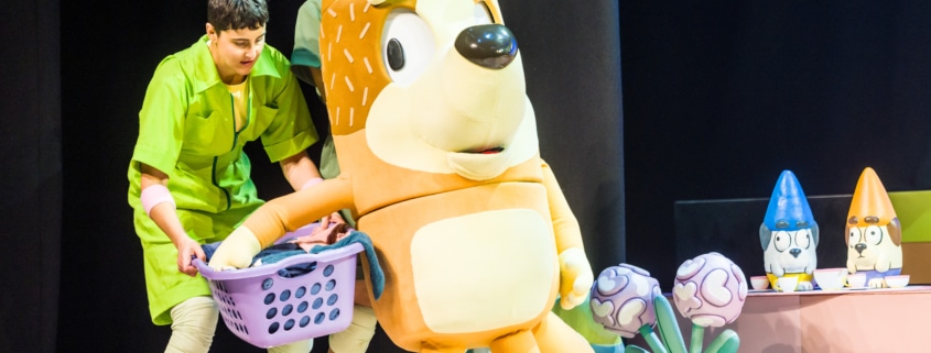 Mum is carrying a laundry basket, supported by actors in green jumpsuits.
