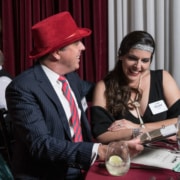 A couple wearing 1920's style costumes is seated at a dinner table, looking over clues