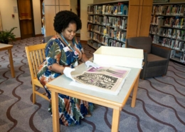 Jameka Lewis seated at a table flips through a large archive book at the Blair Caldwell African American Research Library