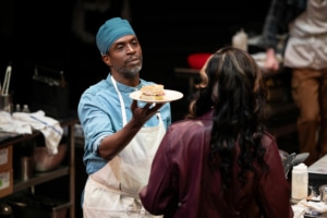 man holds offers a sandwich to a woman with a serene expression on his face.