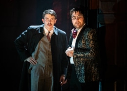 Richard Hannay looks concerned speaking with a man wearing strange glasses and a patterned suit jacket