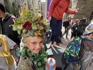 A student wearing an elaborate costume made of leaves and branches smiles during the DPS Shakespeare Festival parade
