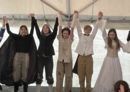 A line of students in costume raise their clasped hands as they take a bow at the DPS Shakespeare Festival