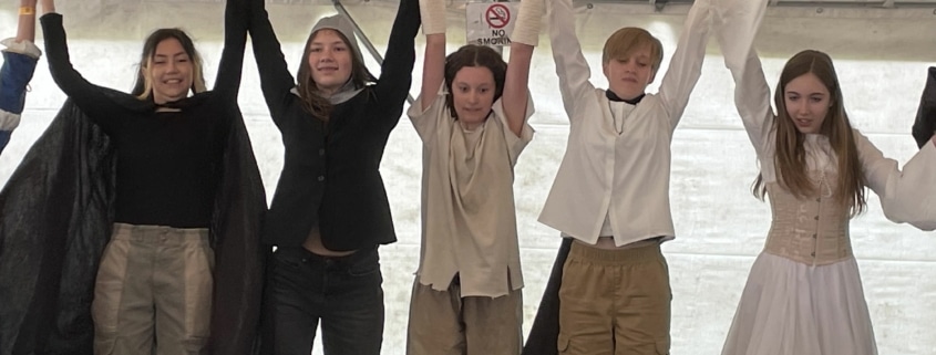 A line of students in costume raise their clasped hands as they take a bow at the DPS Shakespeare Festival