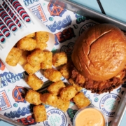 A fried chicken sandwich with a pouch of tater tots spilling on a Birdcall tray