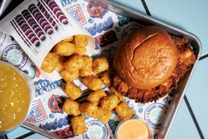 A fried chicken sandwich with a pouch of tater tots spilling on a Birdcall tray
