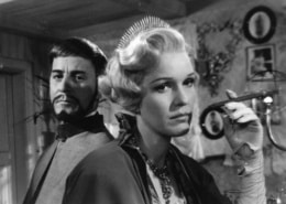 A still from Smiles of a Summer Night. A woman in the forefront raises a hand while a man stands behind her.