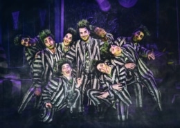 Beetlejuice, wearing his signature black and white striped suit, is surrounded by matching dancers imitating his insane expression