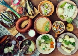 A table filled with several Scandinavian dishes, including a smoked sausage, creamy soup, roasted vegetables, fish, and more