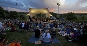 Groups of people sit on the grass outside the Belmar Park amphitheater