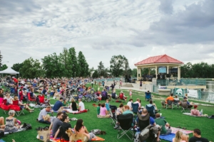 Hundreds of people sit on the grass, on blankets and in chairs. There is a band playing in a small gazebo.