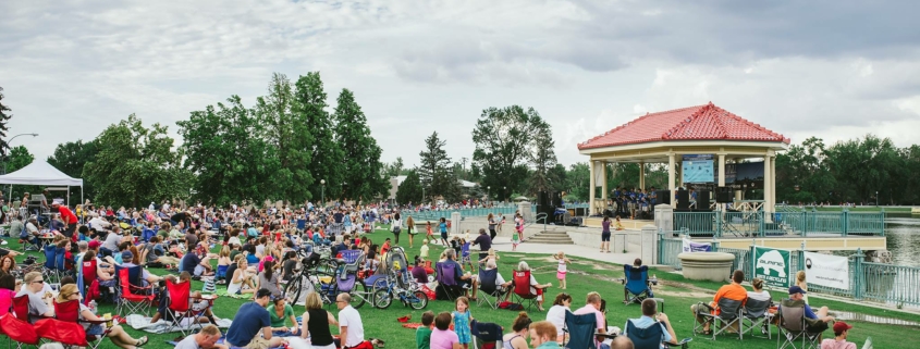 Hundreds of people sit on the grass, on blankets and in chairs. There is a band playing in a small gazebo.