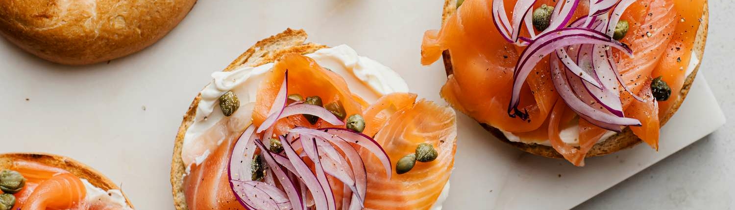 A row of open faced bagels topped with lox, red onion, and capers