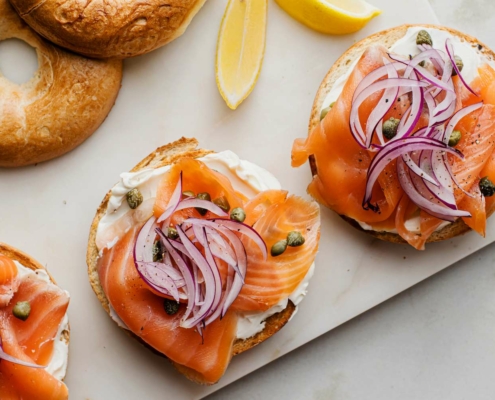 A row of open faced bagels topped with lox, red onion, and capers
