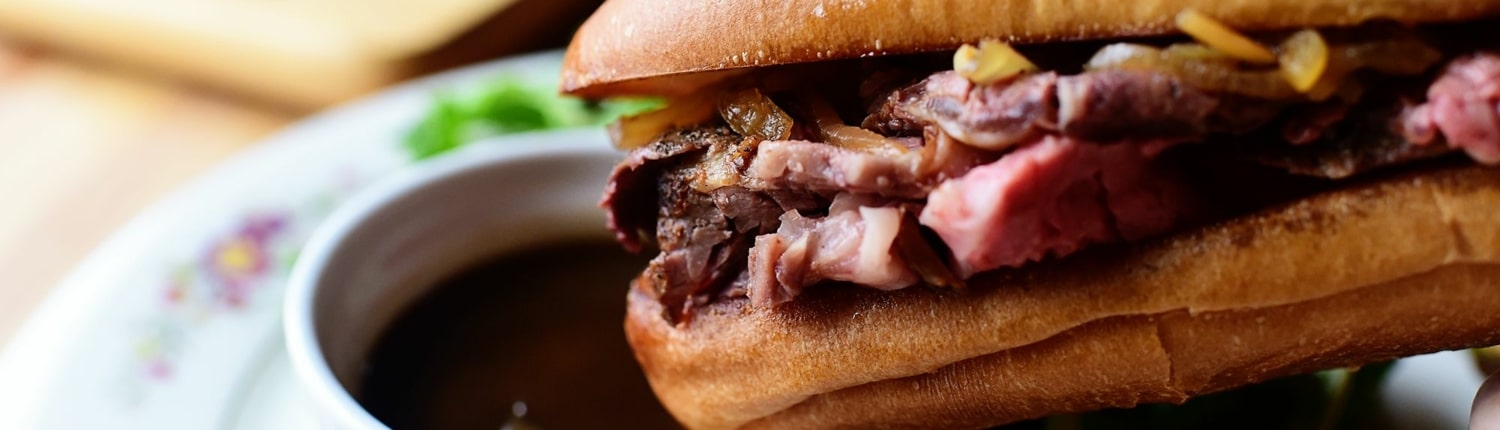 A french dip sandwich about to be dunked into a bowl of drippings