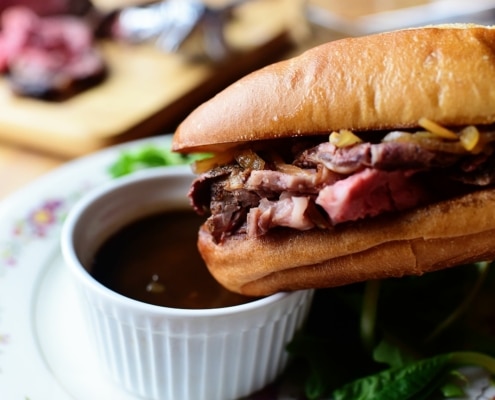 A french dip sandwich about to be dunked into a bowl of drippings