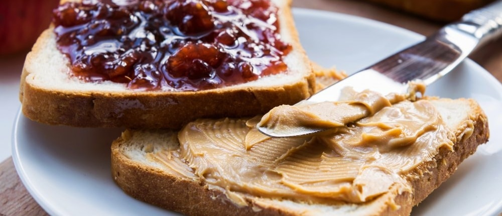 Two slices of bread, each featuring peanut butter and jelly. A butter knife is resting on top.