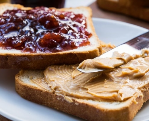 Two slices of bread, each featuring peanut butter and jelly. A butter knife is resting on top.