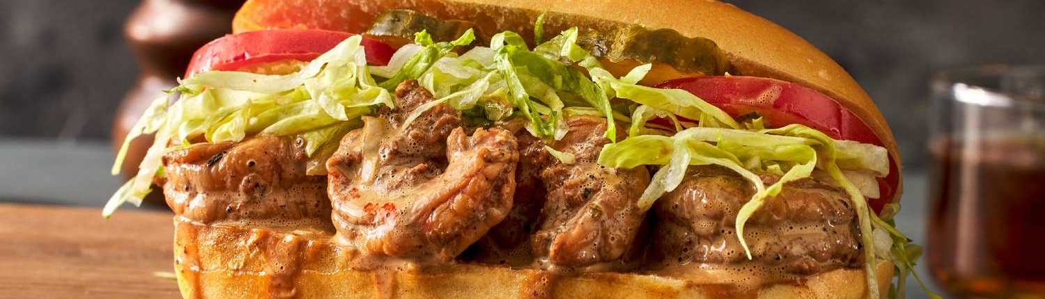 A dressed shrimp po' boy sits on a cutting board. It is dripping gravy