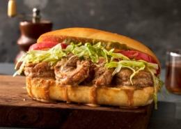 A dressed shrimp po' boy sits on a cutting board. It is dripping gravy