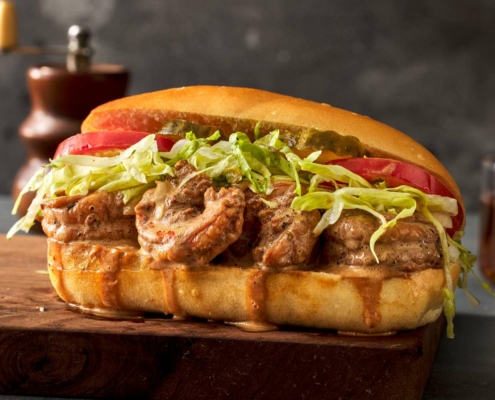 A dressed shrimp po' boy sits on a cutting board. It is dripping gravy