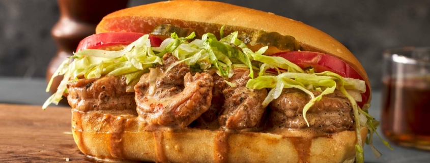 A dressed shrimp po' boy sits on a cutting board. It is dripping gravy