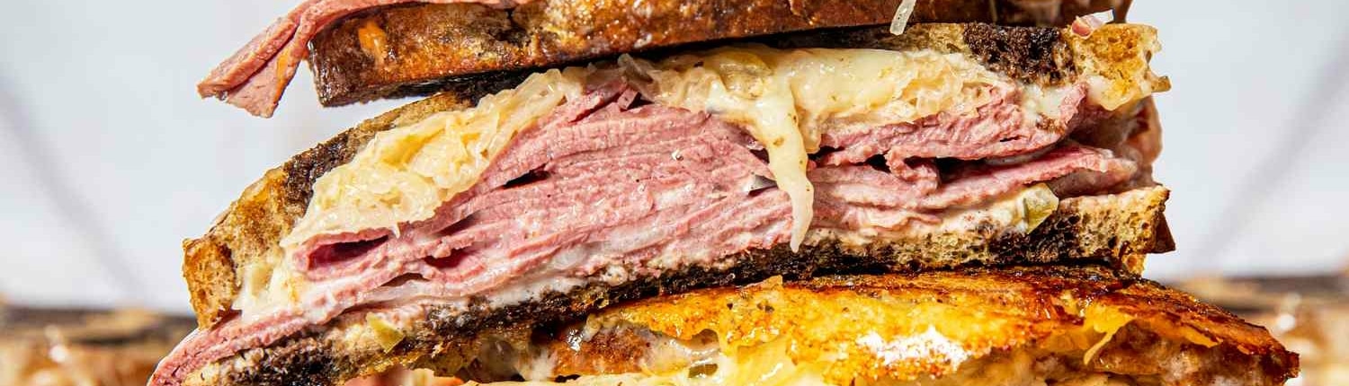 A sliced Reuben sandwich stacked up high. The cheese is melting out of the bread