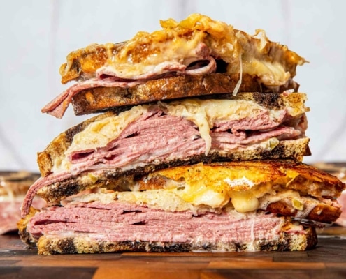 A sliced Reuben sandwich stacked up high. The cheese is melting out of the bread