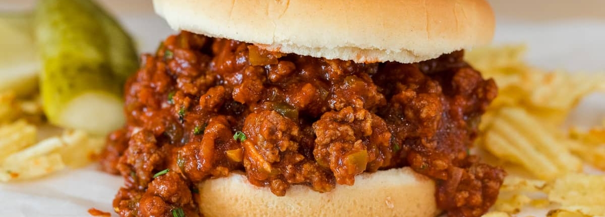 An overflowing sloppy joe sandwich on a simple white hamburger bun.