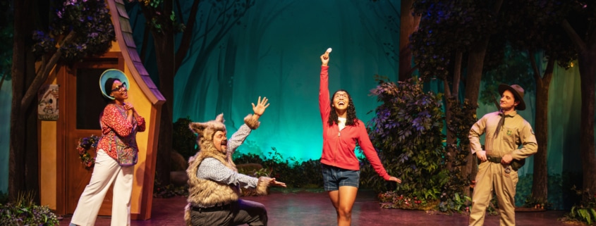Little Red's mom, the Wolf, Little Red, and the Park Ranger sing onstage together. Everyone is looking at Little Red, who stands in the center, smiling.