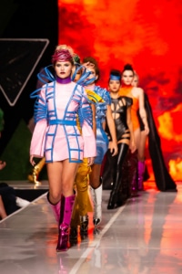 A row of models wearing colorful, structural fashion with cutouts and chunky boots walk the runway